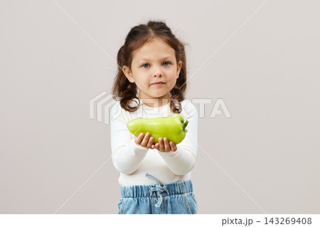 Young girl holding a light green pepper, promoting healthy nutrition, fresh vegetables, and a balanced diet for childhood 143269408