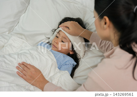 mother applying cold compress on sick daughter's forehead in bed mother applying cold compress on sick daughter's forehead in bed 143269561