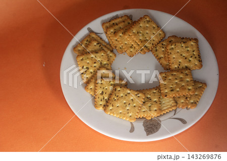 Square Salted Herb Crackers Arranged on White Plate Against Warm Orang 143269876