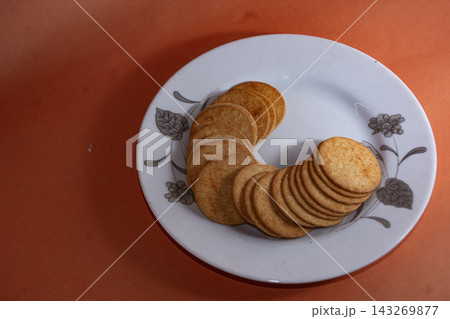 Round Crackers Arranged in Curved Lines on a Floral Pattern Plate with Orange Background Round Crackers Arranged in Curved Lines on a Floral Pattern Plate with Orange Background 143269877