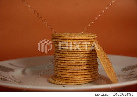 Stacked Crispy Round Crackers on White Ceramic Plate against Warm Orange Background 143269880