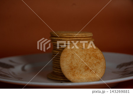 Stack of Golden Round Savory Crackers on a White Plate with Warm Orange Background Stack of Golden Round Savory Crackers on a White Plate with Warm Orange Background 143269881
