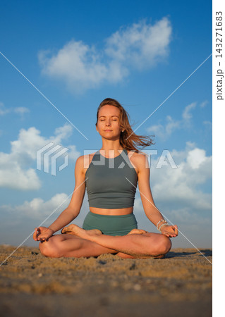 A woman sits in Padmasana yoga, Lotus Pose, with eyes closed and fingers forming Chin Mudra, the Consciousness Seal, on her knees at the beach A woman sits in Padmasana yoga, Lotus Pose, with eyes closed and fingers forming Chin Mudra, the Consciousness Seal, on her knees at the beach 143271683