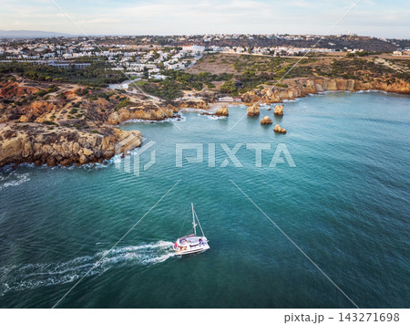 Aerial view of Praia dos Arrifes in warm evening light with golden cliffs, rocky islets and green Atlantic water. Aerial view of Praia dos Arrifes in warm evening light with golden cliffs, rocky islets and green Atlantic water. 143271698