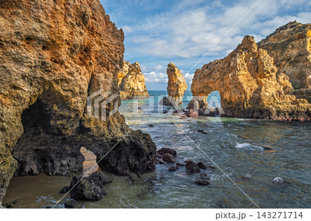Ground-level view from a rocky cove at Ponta da Piedade in Lagos, Algarve, Portugal, with a natural sea arch, limestone rock towers and calm blue water. Ground-level view from a rocky cove at Ponta da Piedade in Lagos, Algarve, Portugal, with a natural sea arch, limestone rock towers and calm blue water. 143271714