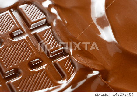 Thick warm chocolate waves flooding over solid chocolate bar close up 143273404