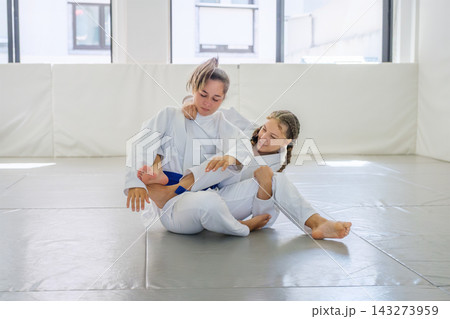 Two Brazilian jiu jitsu students practice a bow and arrow choke setup as one holds the collar and pants near the knee while leaning sideways Two Brazilian jiu jitsu students practice a bow and arrow choke setup as one holds the collar and pants near the knee while leaning sideways 143273959
