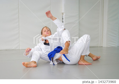 A Brazilian jiu jitsu student maintains a collar choke grip from behind as her partner raises an arm and turns on the tatami 143273960
