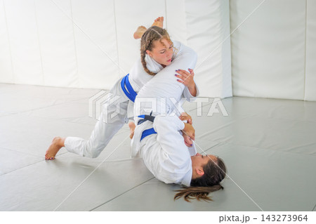 A Brazilian jiu jitsu student stays on her knees while controlling the legs during a guard pass drill on the tatami A Brazilian jiu jitsu student stays on her knees while controlling the legs during a guard pass drill on the tatami 143273964