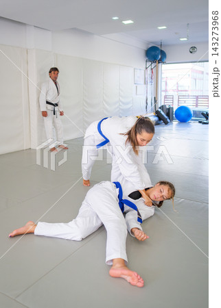 Female martial artists finish uchi-mata, the judo inner thigh reaping throw, during Brazilian jiu jitsu (BJJ) training while maintaining arm control as an instructor watches Female martial artists finish uchi-mata, the judo inner thigh reaping throw, during Brazilian jiu jitsu (BJJ) training while maintaining arm control as an instructor watches 143273968