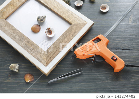 Orange glue gun workspace seashell frame decoration background. Hot melt adhesive tool hobby creative activity. DIY home decor handmade room improvement project. 143274402