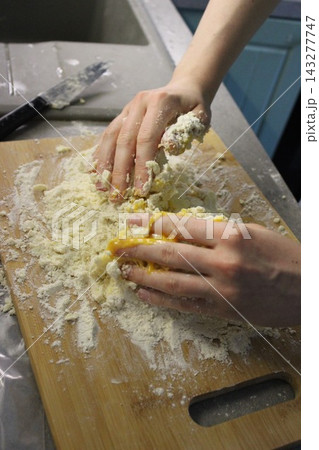 Hands mixing flour and egg on a wooden cutting board in a kitchen, with a stainless steel sink and blue cabinetry visible in the background 143277747