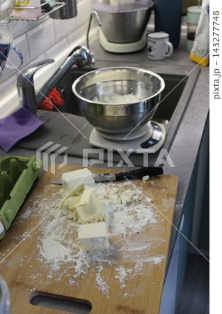 Kitchen countertop with scattered flour, butter cubes, and a mixing bowl on a scale, showcasing baking preparation in a modern home kitchen environment 143277748