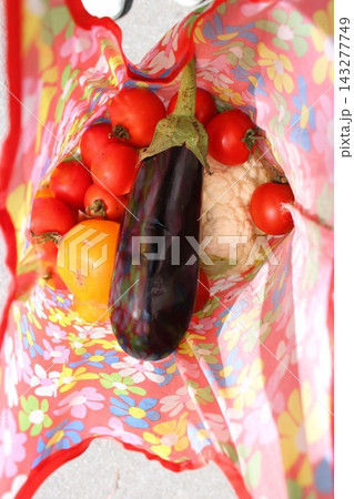 Colorful reusable bag filled with fresh vegetables including tomatoes, eggplant, and cauliflower on a light surface, showcasing vibrant produce and eco-friendly shopping Colorful reusable bag filled with fresh vegetables including tomatoes, eggplant, and cauliflower on a light surface, showcasing vibrant produce and eco-friendly shopping 143277749