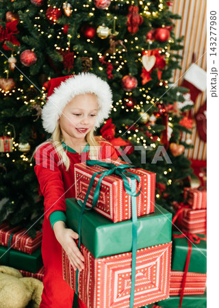 Merry Christmas and Happy Holidays. Child girl in Santa Claus hat with gifts under Christmas tree Merry Christmas and Happy Holidays. Child girl in Santa Claus hat with gifts under Christmas tree 143277980