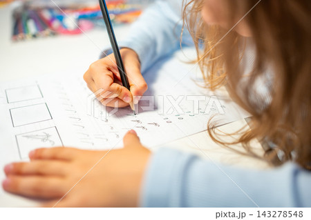 First grade girl practices handwriting with pencil in school workbook. Child learns to write letters during early education with selective focus and shallow depth of field First grade girl practices handwriting with pencil in school workbook. Child learns to write letters during early education with selective focus and shallow depth of field 143278548