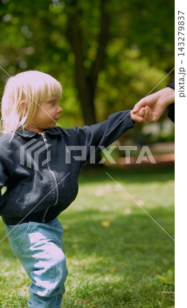 Toddler with light hair takes cautious steps guided by gentle hand in park 143279837