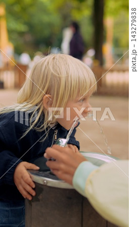 Cheerful toddler playing and drinking water outside with family Cheerful toddler playing and drinking water outside with family 143279838