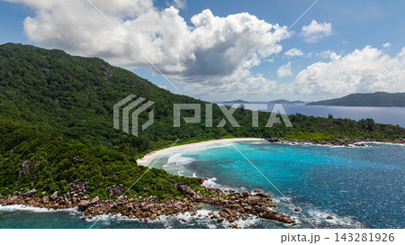 Green hills overlooking a white sandy beach with turquoise ocean waves and blue sky. Petite Anse. Seychelles, La Digue. 143281926