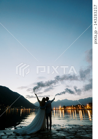 Happy couple marked by glowing lights embracing under dusk sky with smoke plume Happy couple marked by glowing lights embracing under dusk sky with smoke plume 143283217