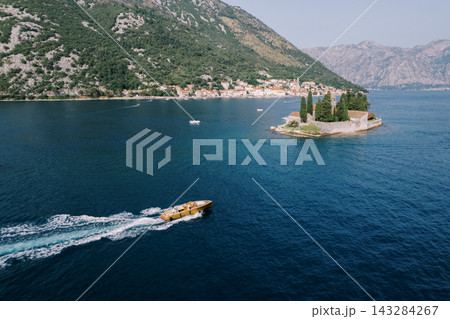 Swift speedboat rushes by tiny church island amid scenic mountain backdrop and calm waters Swift speedboat rushes by tiny church island amid scenic mountain backdrop and calm waters 143284267