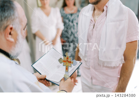 Priest Holding Cross and Book During Religious Ceremony 143284380