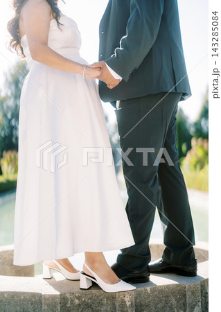 Sunlit wedding hands. Romantic outdoor wedding with bride in teal dress and groom in dark suit Sunlit wedding hands. Romantic outdoor wedding with bride in teal dress and groom in dark suit 143285084