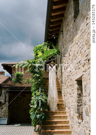Charming wedding dress gracefully draped on rustic stone steps under leafy balcony canopy Charming wedding dress gracefully draped on rustic stone steps under leafy balcony canopy 143285179