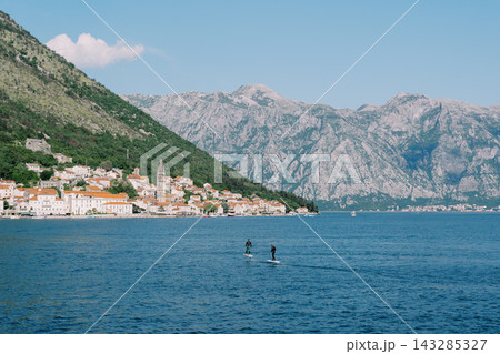 Adventurous paddleboard enthusiasts navigate radiant coastal landscapes with geological features 143285327
