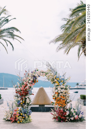 Intimate wedding setup on coast with pastel floral arch and tranquil water background 143285440
