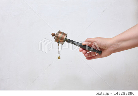 A human hand holds a traditional Tibetan prayer wheel against a light background. A human hand holds a traditional Tibetan prayer wheel against a light background. 143285890