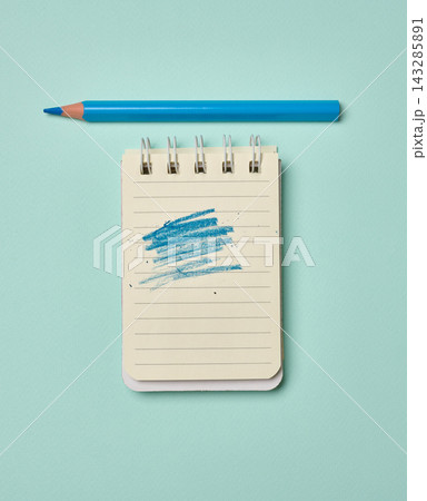 Spiral-bound lined notepad with a blue scribbled stroke and a blue pencil on a turquoise background. 143285891