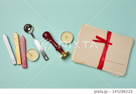 Vintage postcard, stack of letters with a red ribbon, candle, pencil, and wax seal on a turquoise background 143286228