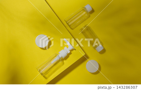 A set of transparent plastic bottles and jars with white lids on a yellow background A set of transparent plastic bottles and jars with white lids on a yellow background 143286307