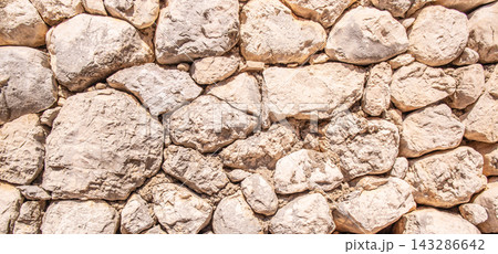 Textured stone wall composed of irregularly shaped light-colored rocks arranged closely together, creating a natural and rustic appearance in a dry environment Textured stone wall composed of irregularly shaped light-colored rocks arranged closely together, creating a natural and rustic appearance in a dry environment 143286642