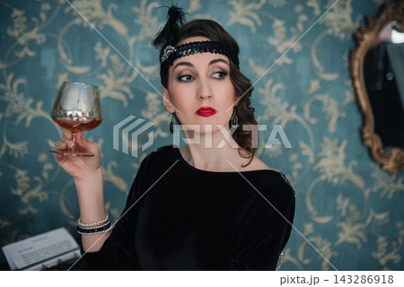 Elegant girl in black flapper dress holding a glass of cognac Elegant girl in black flapper dress holding a glass of cognac 143286918