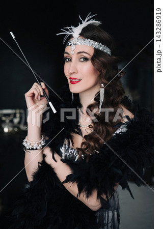 Elegant girl in 1920s flapper outfit holding a long cigarette holder Elegant girl in 1920s flapper outfit holding a long cigarette holder 143286919