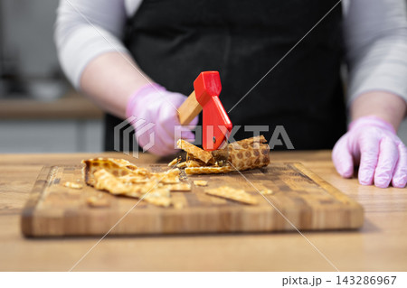 Confectioner crushing a wafer roll with a creative axe-shaped pizza cutter Confectioner crushing a wafer roll with a creative axe-shaped pizza cutter 143286967