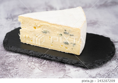 Wedge of creamy blue-veined brie on a black slate board Wedge of creamy blue-veined brie on a black slate board 143287209