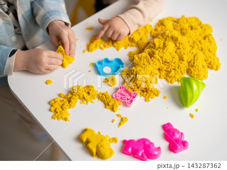 Children playing with yellow kinetic sand and colorful plastic molds Children playing with yellow kinetic sand and colorful plastic molds 143287362