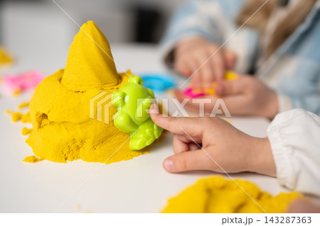 Children playing with yellow kinetic sand and colorful plastic molds Children playing with yellow kinetic sand and colorful plastic molds 143287363