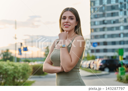 Smiling young woman touching her chin posing outdoors near modern building Smiling young woman touching her chin posing outdoors near modern building 143287797