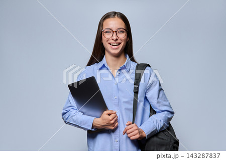 Laughing female student holding laptop and backpack on gray studio background 143287837