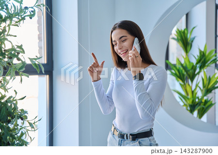 Pleasant young woman speaking on smartphone looking away indoors 143287900