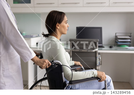Female doctor in white coat pushing young woman in wheelchair Female doctor in white coat pushing young woman in wheelchair 143289456