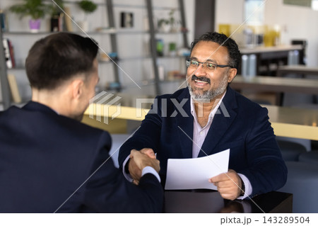 Smiling hr manager holds resume paper handshakes with male applicant Smiling hr manager holds resume paper handshakes with male applicant 143289504