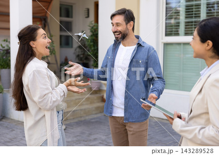Excited couple celebrating buying house laughing tossing keys into air 143289528