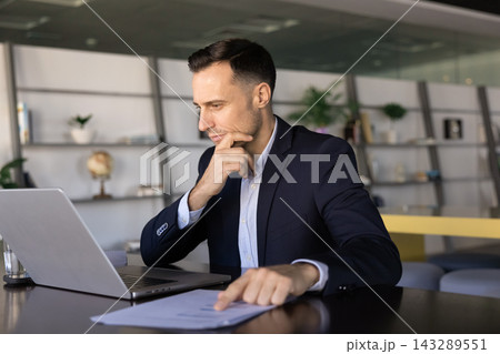 Focused businessman reviewing printed charts thoughtfully at office desk 143289551
