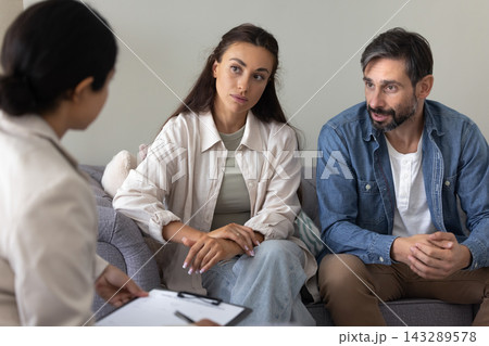 Serious married couple sitting on sofa talking to female psychologist Serious married couple sitting on sofa talking to female psychologist 143289578