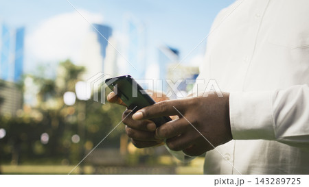 Close up of man holding smartphone and scrolling on website in sunny public park, using internet and social media on mobile phone. Technology use everyday life. Close up of man holding smartphone and scrolling on website in sunny public park, using internet and social media on mobile phone. Technology use everyday life. 143289725
